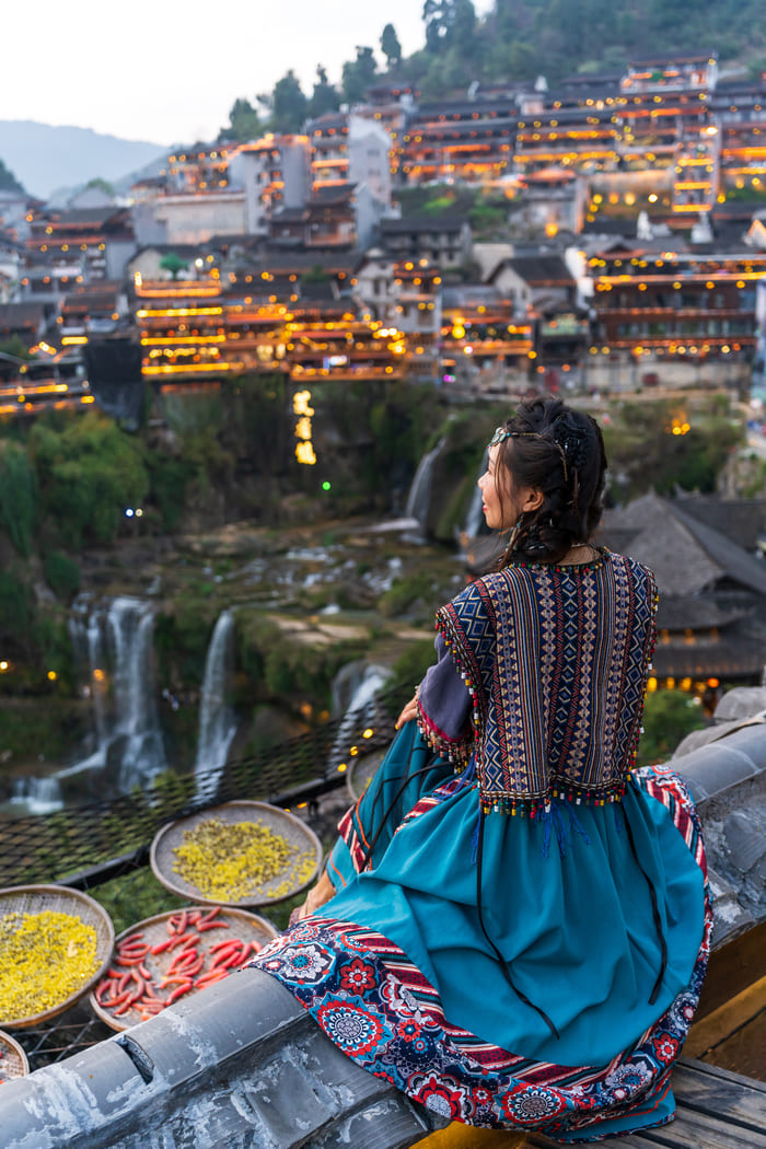 Foto de una chica sentada a la orrilla de un risco en la ciudad de Lijiang